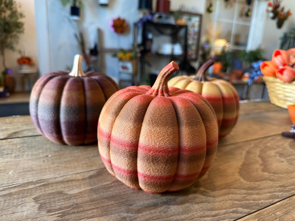 Three large 3D printed pumpkins in multicolor rustic fall finishes displayed on a wooden table at AO3D.